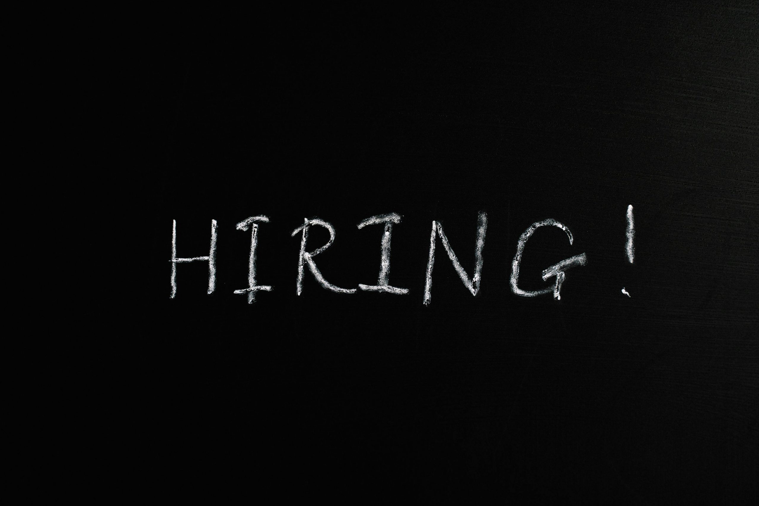 We are hiring! Close-up of the word 'Hiring!' written in white chalk on a blackboard, ideal for recruitment themes.